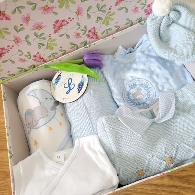 Caixa floral com roupa de bebé azul e acessórios de malha