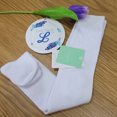 Meia-calça infantil branca com etiquetas perto de flor roxa sobre mesa de madeira