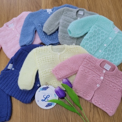 Casacos de malha de bebé em várias cores sobre mesa de madeira com duas tulipas roxas