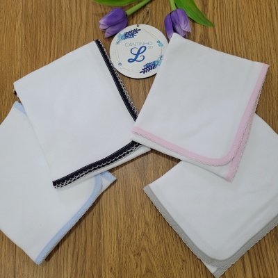 Quatro panos brancos com bordas coloridas em azul claro, azul escuro, rosa e cinza sobre madeira, com rótulo redondo e flores roxas.