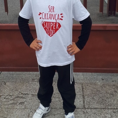 Criança com t-shirt branca com texto vermelho, calças e ténis brancos ao ar livre