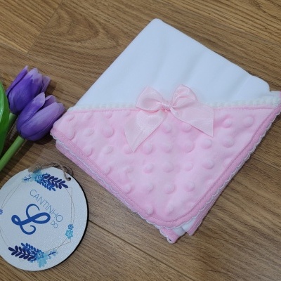 Manta para bebé branca e rosa com laço e etiqueta CANTINHO L sobre madeira com tulipas roxas