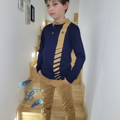 Menino com camisa azul escura com detalhes dourados e calças douradas numa escadaria interior