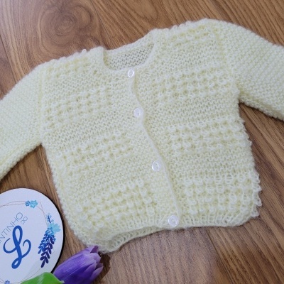 Casaco de malha bege claro para bebé com botões brancos sobre madeira clara