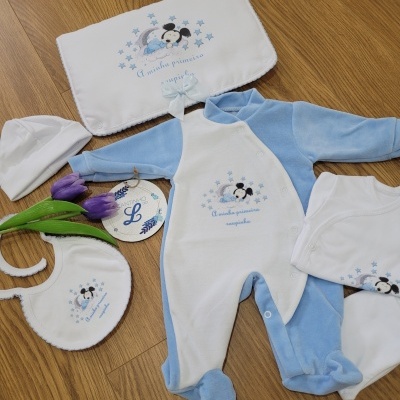 Conjunto de roupa de bebé azul e branca com ursinho bordado e texto, decorado com tulipas roxas, em chão de madeira