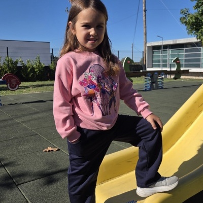 Menina com casaco rosa e estampa de personagens numa escorrega amarela em parque infantil