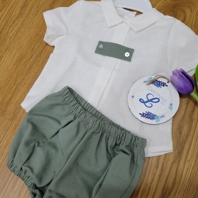 Conjunto de roupa para bebé com camisa branca e calções verdes sobre superfície de madeira