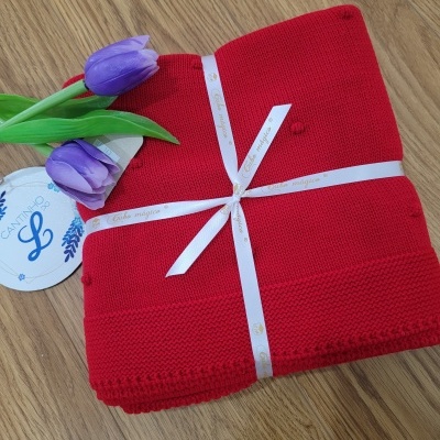 Cobertor vermelho tricotado com fita branca, flores roxas e etiqueta circular