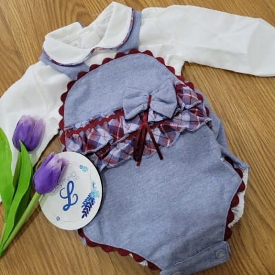 Macacão de bebé azul com faixa xadrez e laço, tag 'L' e tulipas roxas sobre madeira