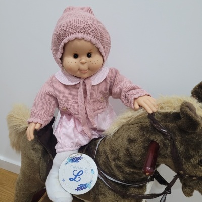 Boneca de pano vestida de rosa num cavalo de brinquedo de pelúcia castanho com crina bege