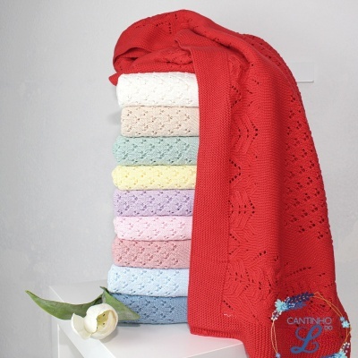 Pilha de roupa de malha colorida com padrão de pontos vazados sobre superfície branca com flor e logotipo CANTINHO L