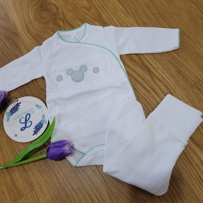 Conjunto de roupa de bebé branca com bordas verdes e padrão Mickey bordado colocado em madeira com flor roxa e cartão redondo