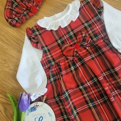 Conjunto infantil com vestido xadrez vermelho, camisa branca e gorro xadrez sobre madeira com flores lilás