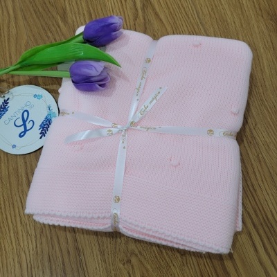 Manta bebê cor-de-rosa clara com flores roxas em superfície de madeira