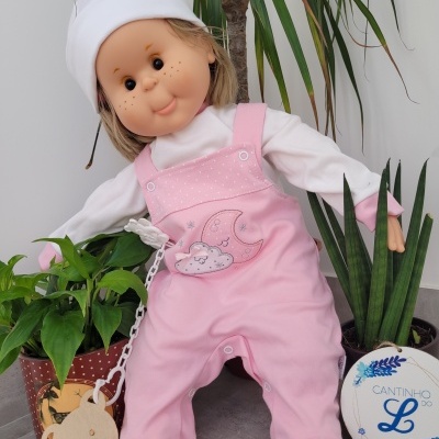 Boneca com roupa rosa e branca entre plantas, ao lado de círculo decorativo com texto.