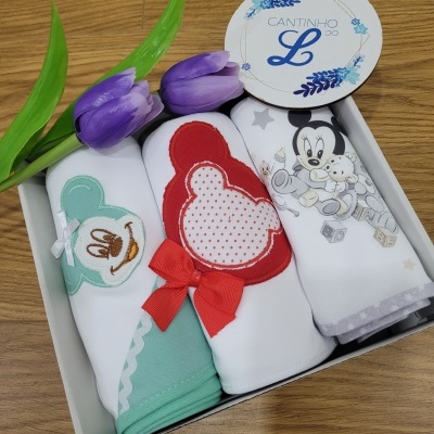 Conjunto de três fraldas com personagens Disney em caixa branca com flores roxas e etiqueta redonda