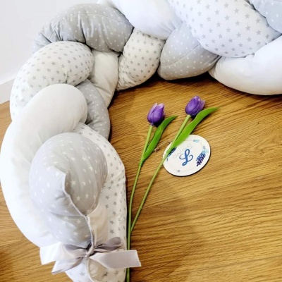 Almofada trançada cinza e branca com estrelas, flores roxas e cartão 'L' sobre madeira