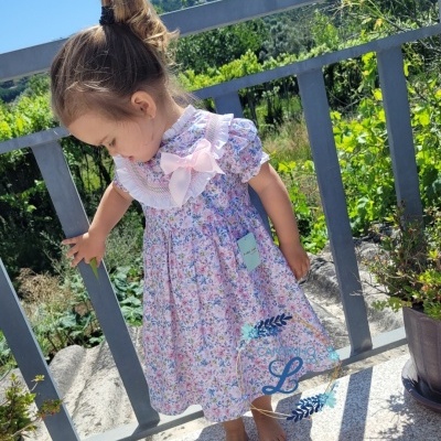 Criança com vestido floral colorido com gola de renda e laço cor-de-rosa ao ar livre