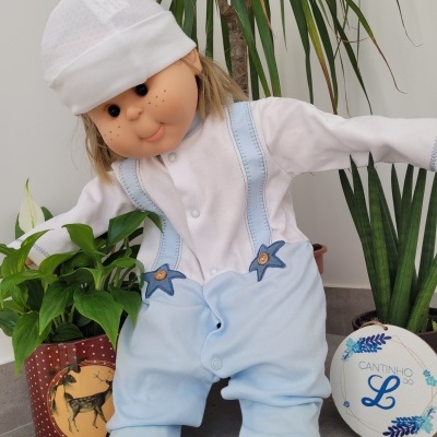 Boneco de tecido com roupa branca e azul clara entre plantas em vasos