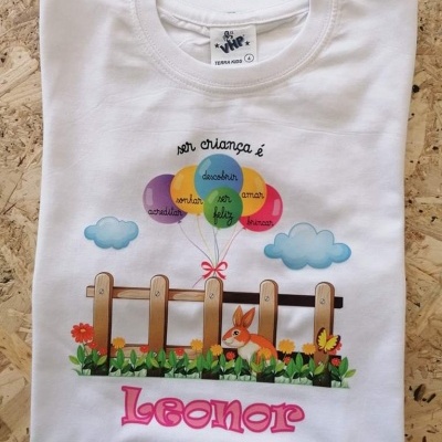Camisola branca com desenho de coelho, cerca, flores, balões e texto em português
