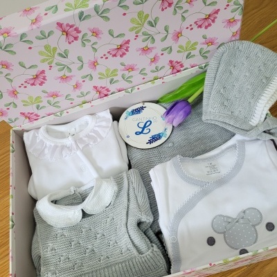 Caixa de presente para bebê com roupinhas cinza e branco, tulipa roxa e cartão branco azul.