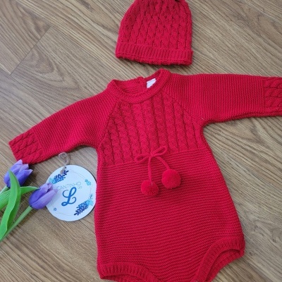 Conjunto de bebé vermelho em malha com camisola e gorro, sobre chão de madeira