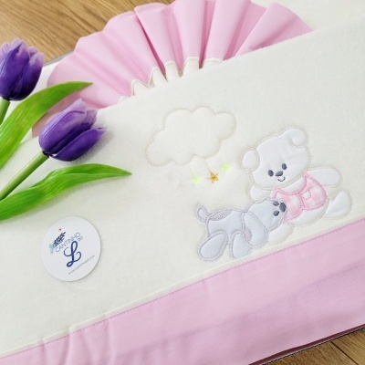 Capa de tecido branca com ursinhos bordados e faixa rosa, flores roxas e etiqueta redonda.