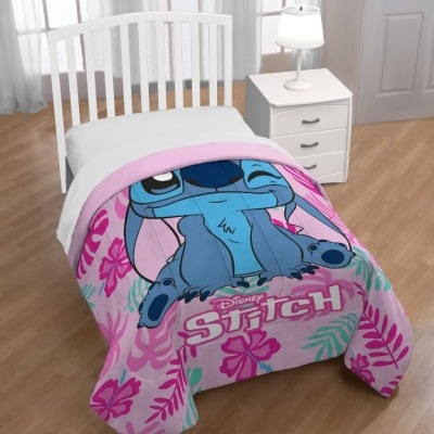 Colcha infantil estampada com Stitch da Disney em cama branca num quarto com mesa e candeeiro