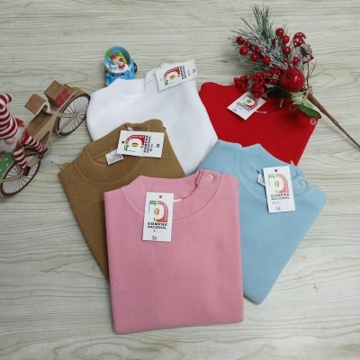 Camisolas de malha coloridas com etiquetas da marca CAMEPA alinhadas sobre uma superfície de madeira clara com decoração natalícia ao lado.