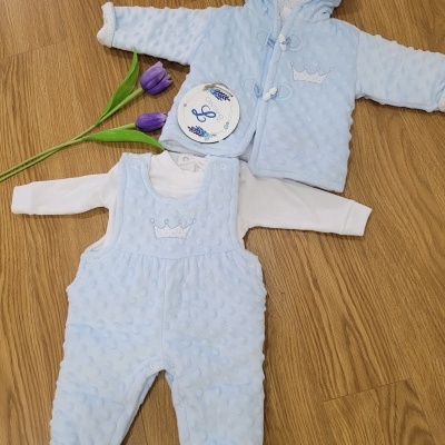 Conjunto de roupa de bebé azul com casaco e jardineiras, sobre chão de madeira.