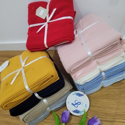 Conjunto de mantas de malha dobradas em várias cores com fita branca, etiqueta redonda e flores roxas