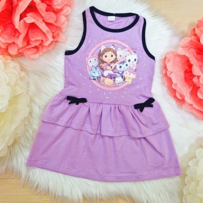 Vestido infantil lilás com estampa de menina e animais, laços pretos, sobre fundo felpudo branco com flores de papel.