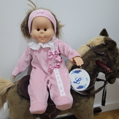 Boneca de pano com pijama rosa sentada num cavalo de balanço castanho de tecido