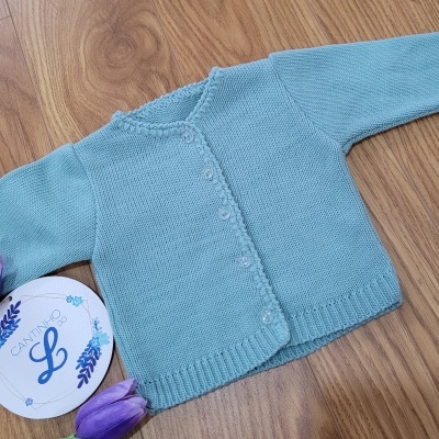 Cardigan azul claro de malha com botões sobre madeira, junto a duas tulipas roxas e disco decorativo