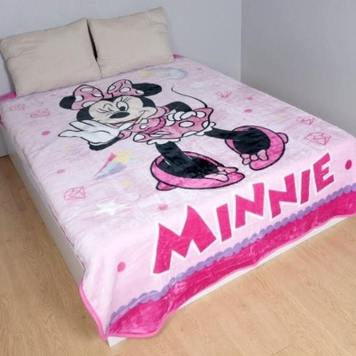 Cobertor infantil rosa com desenho da Minnie Mouse e texto MINNIE numa cama