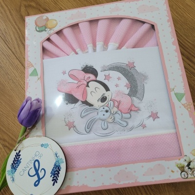 Caixa decorativa com roupa de bebé rosa e imagem de Minnie Mouse com coelho, sobre superfície de madeira com flor roxa