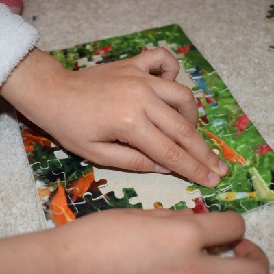 Mãos infantis montam um puzzle com peças coloridas sobre chão branco.