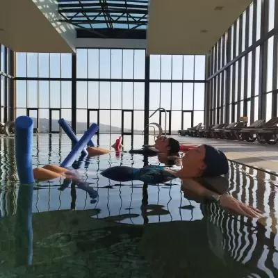 Piscina interior com teto de vidro e pessoas relaxando com boias azuis