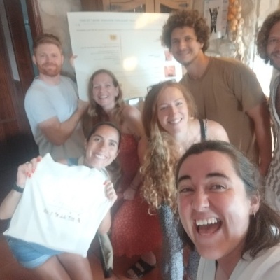 Grupo de seis pessoas numa sala, uma segura uma t-shirt branca com texto