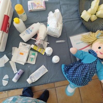 Kit primeiros socorros, medicamentos, boneca de pano azul e melão em prato cinza sobre superfície azul.