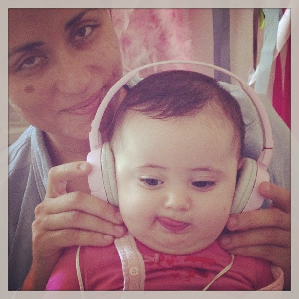 Bebé com auscultadores brancos e cor-de-rosa acolchoados, segurado por adulto.