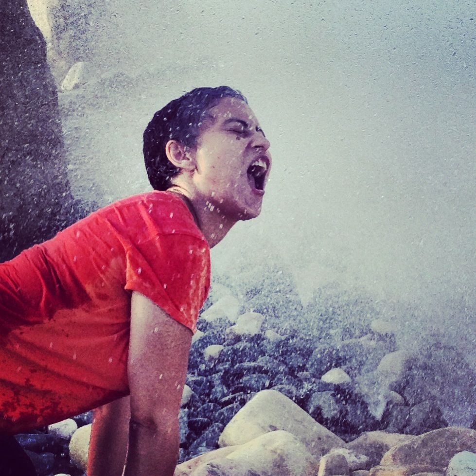 Criança de camiseta vermelha entre rochas com água em spray