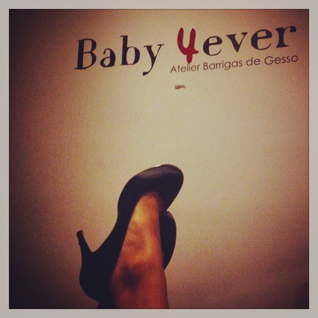 ADRENALINA VS TÓXINA Perna com sapato de salto alto preto e parede com texto 'Baby Fever Atelier Barrigas de Gesso'