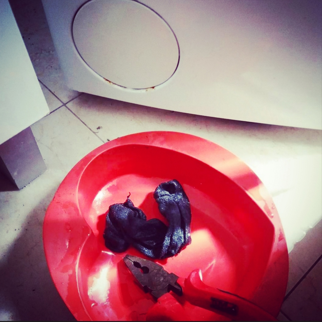 Bacia vermelha em forma de coração com saco plástico preto e alicate no chão de azulejo