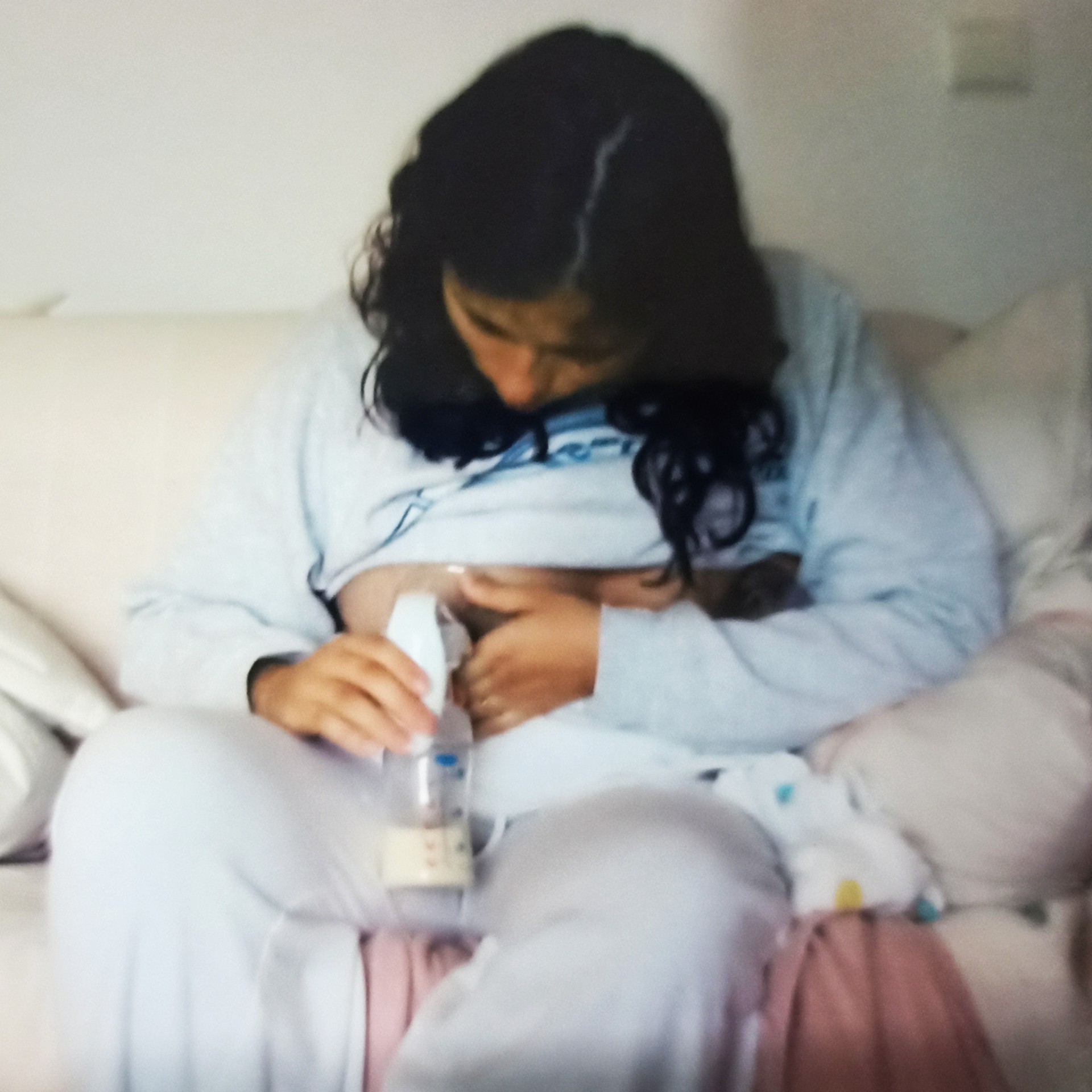 Mulher em roupa cinza a alimentar bebé com biberão sentado no colo