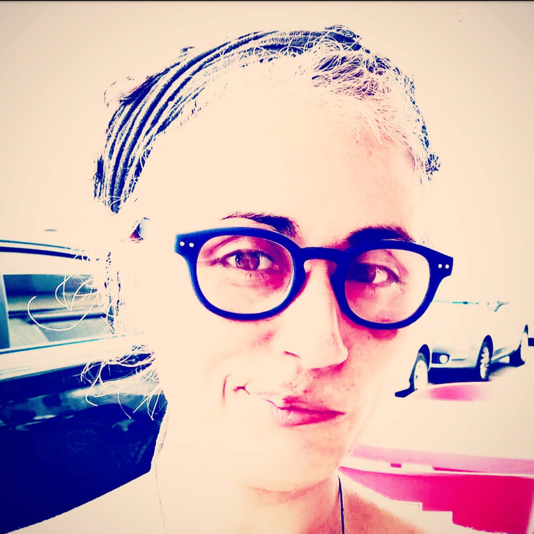 Mulher com óculos redondos pretos em ambiente exterior com carros e mesas vermelhas