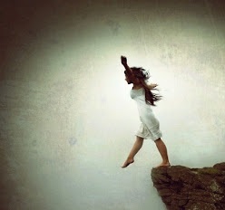 Mulher de vestido branco a saltar de uma rocha contra céu nublado