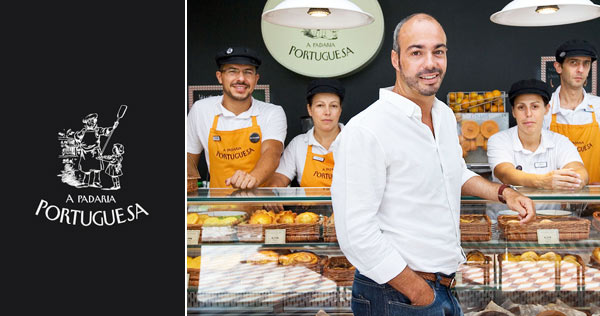 Funcionários de padaria uam aventais amarelos e homem em camisa branca diante de vitrine com pães