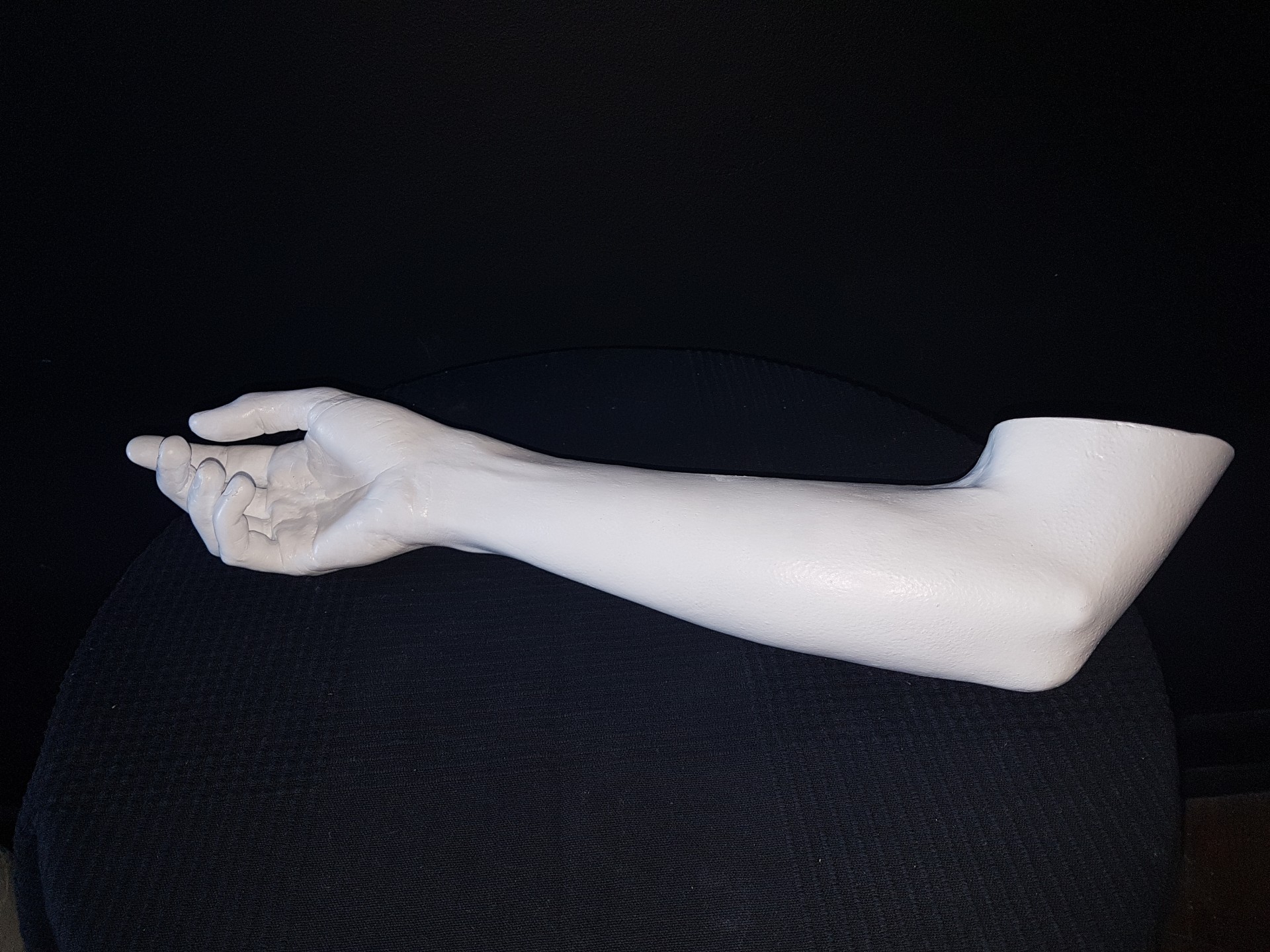 Braço direito de manequim branco sobre superfície preta e fundo escuro