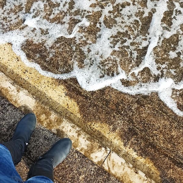 Botas pretas em couro sobre superfície áspera junto a água com espuma